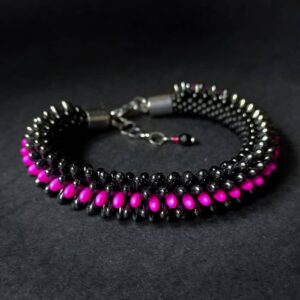 Immagine rappresenta sullo sfondo nero un braccialetto fatto a mano con perline di vetro allungate, nere, fuchsia e grigio metallico. Chiusura in acciaio chirurgico anallergico.